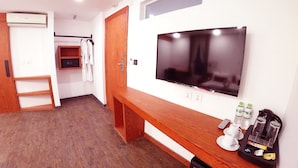 Habitación de hotel con un banco de madera, un televisor de pantalla plana, un armario y un estante pequeño con artículos de aseo.