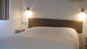 A neatly made bed with a wooden headboard, two bedside tables, and wall-mounted lights. - Mobil-Home 4 people comfort n°27 (Gonneville en Auge)