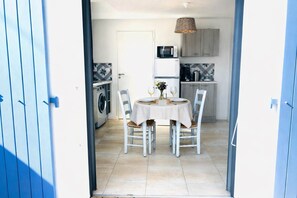 A dining area with a table set for two, a washing machine, and kitchen cabinets. - LE LOGIS, Gîte 1. Clos des Aigrettes, 30m from La Cotinière Port. (Saint-Pierre-d'Oléron)