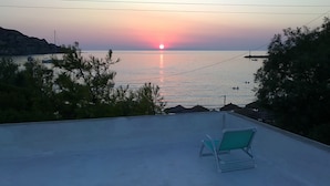 Katto, jolta avautuu näkymä auringonlaskuun meren yllä, siellä on myös tuoli ja muutamia puita.