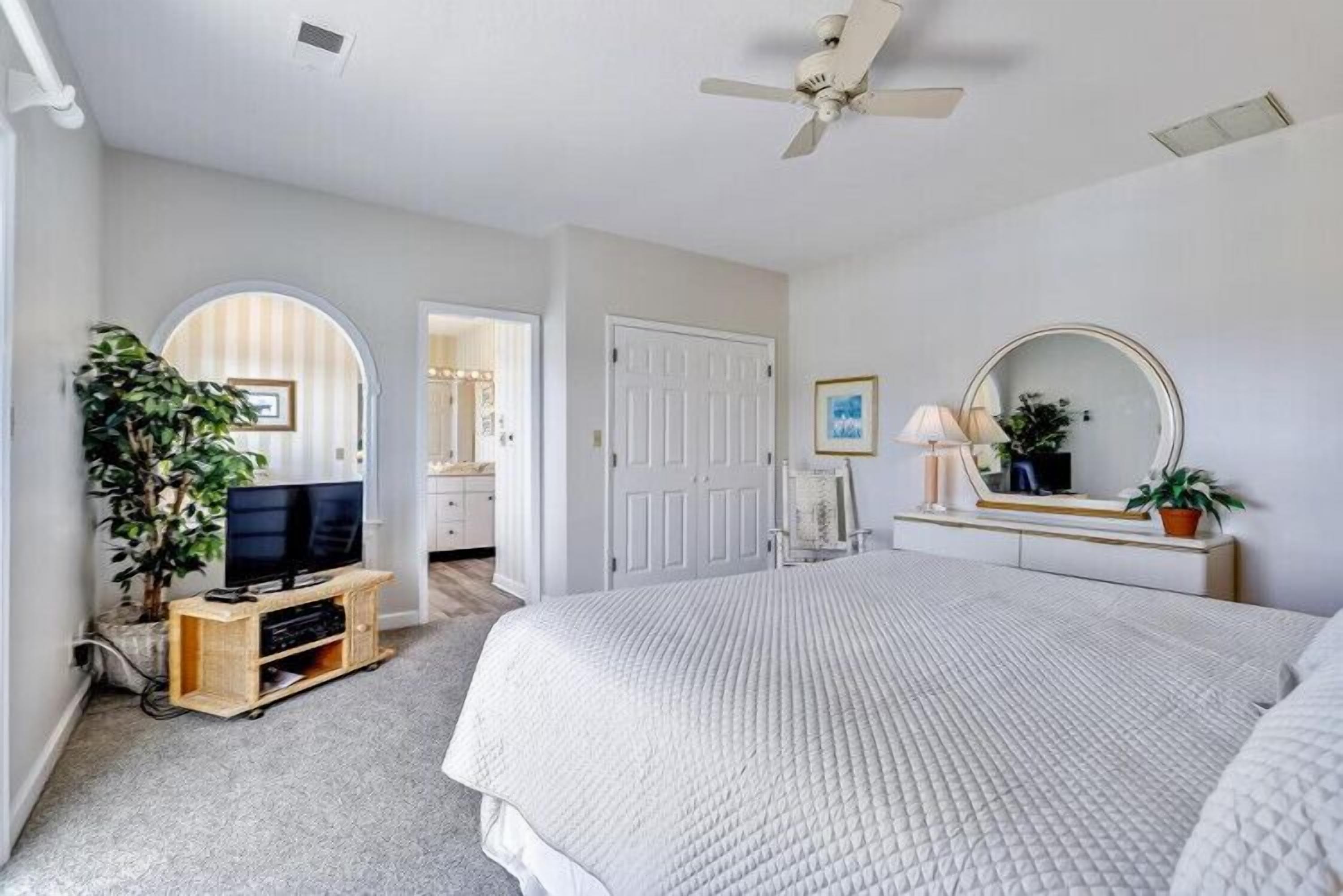 A bedroom with a bed, a television, a ceiling fan, a dresser, and a mirror.