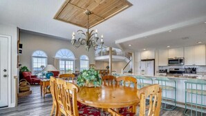 A spacious dining area with a wooden table and chairs, a chandelier, and a view of the kitchen and living room.
