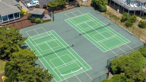 An aerial view of a tennis court complex with multiple courts, surrounded by trees and buildings.