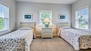 A bedroom with two beds, a nightstand with a lamp, and two framed pictures on the wall.