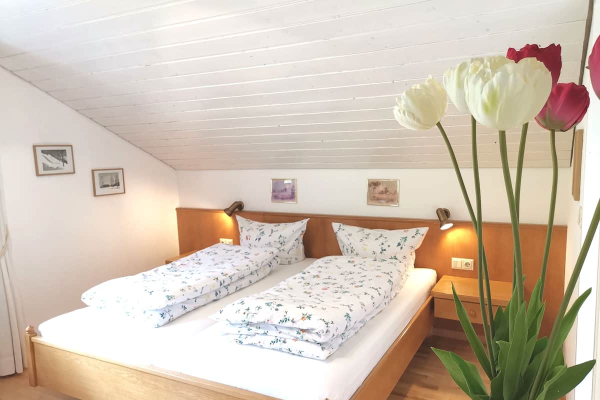 Ein Doppelbett mit floraler Bettwäsche, ein Holzkopfende, Nachttischlampen und ein Blumentopf mit Tulpen.