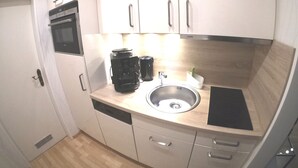 Een compacte keuken met witte kastjes, een vaatwasser, een koffiezetapparaat en een spoelbak.