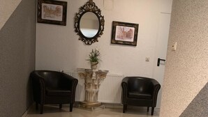 A staircase with red carpet runners leading up to a landing with two black leather chairs and a decorative vase with a plant. - Pension Nathalie Leser (Baden-Baden)
