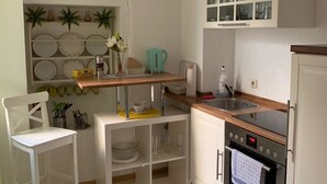 A compact kitchen with white cabinetry, a wooden countertop, a sink, an oven, and a small dining area with a chair. - Pension Nathalie Leser (Baden-Baden)