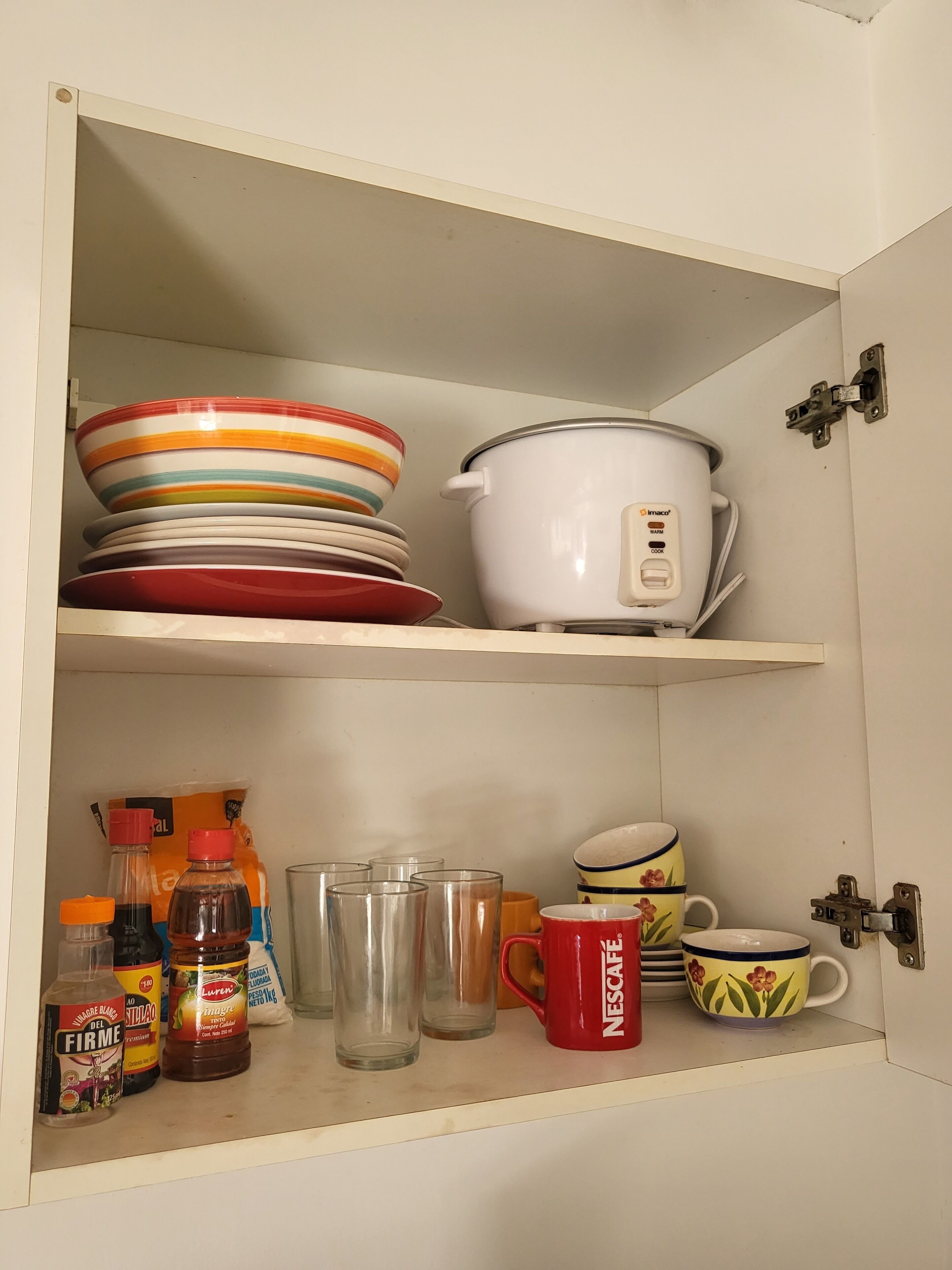 Un pensile della cucina con ripiani che contengono piatti colorati, un pentacotto bianco e diversi oggetti da cucina come bottiglie e bicchieri.