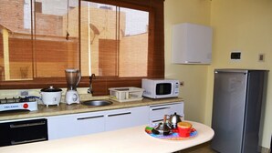 A kitchen with a gas stove, microwave, refrigerator, and a window with blinds.