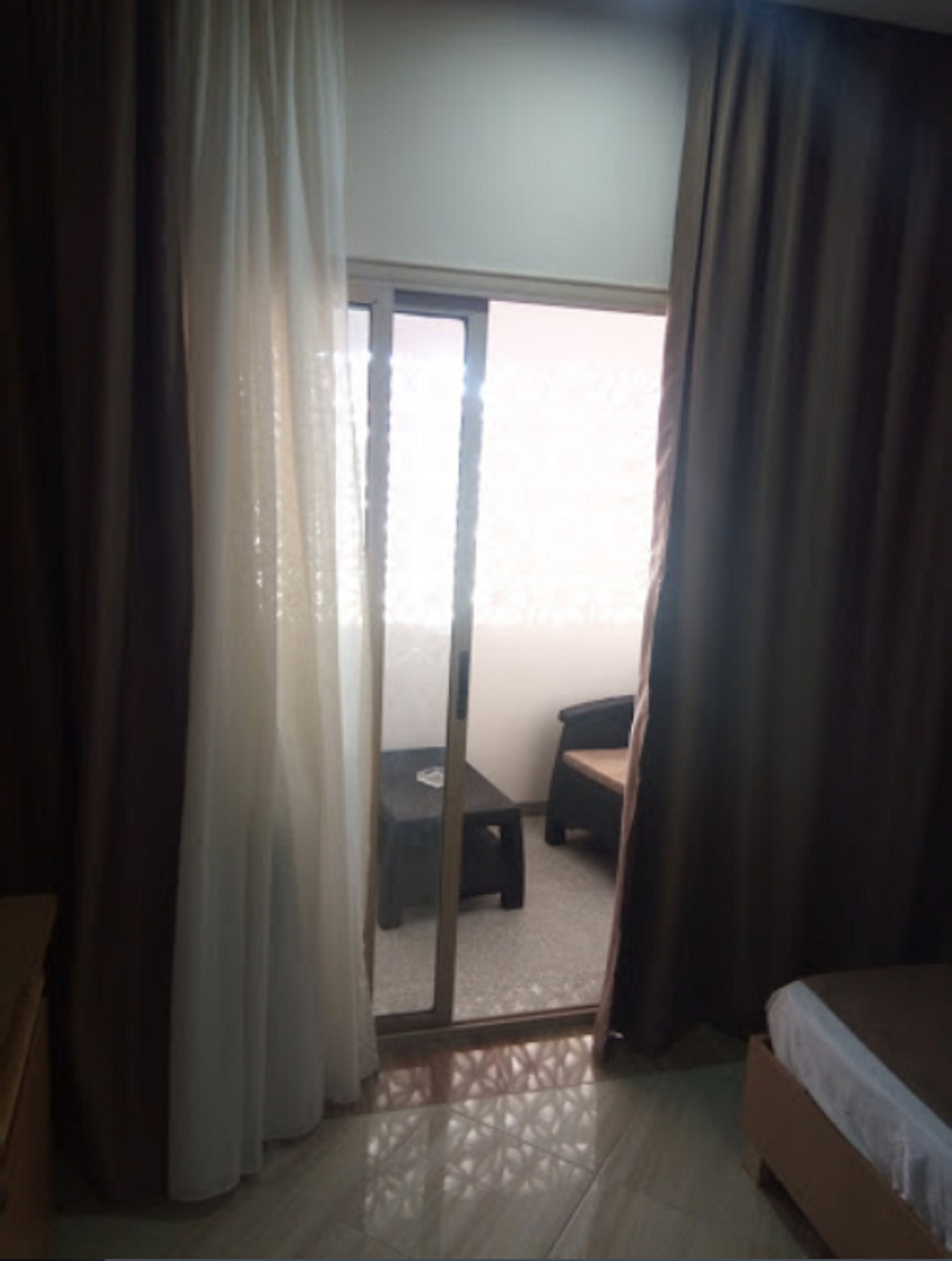 Ein Hotelzimmer mit Bett, einem kleinen Tisch und einem Stuhl. Eine Schiebetür öffnet sich zu einem Außenbereich.