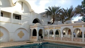 A swimming pool with a tiled deck, surrounded by white walls with arches and decorative elements. - Hotel Souf (El Oued)