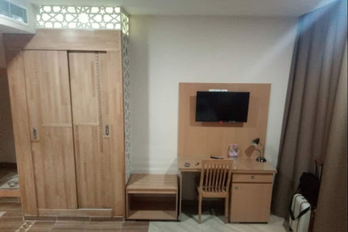 Un dormitorio con un armario de madera, un escritorio con silla, televisor y una cama.