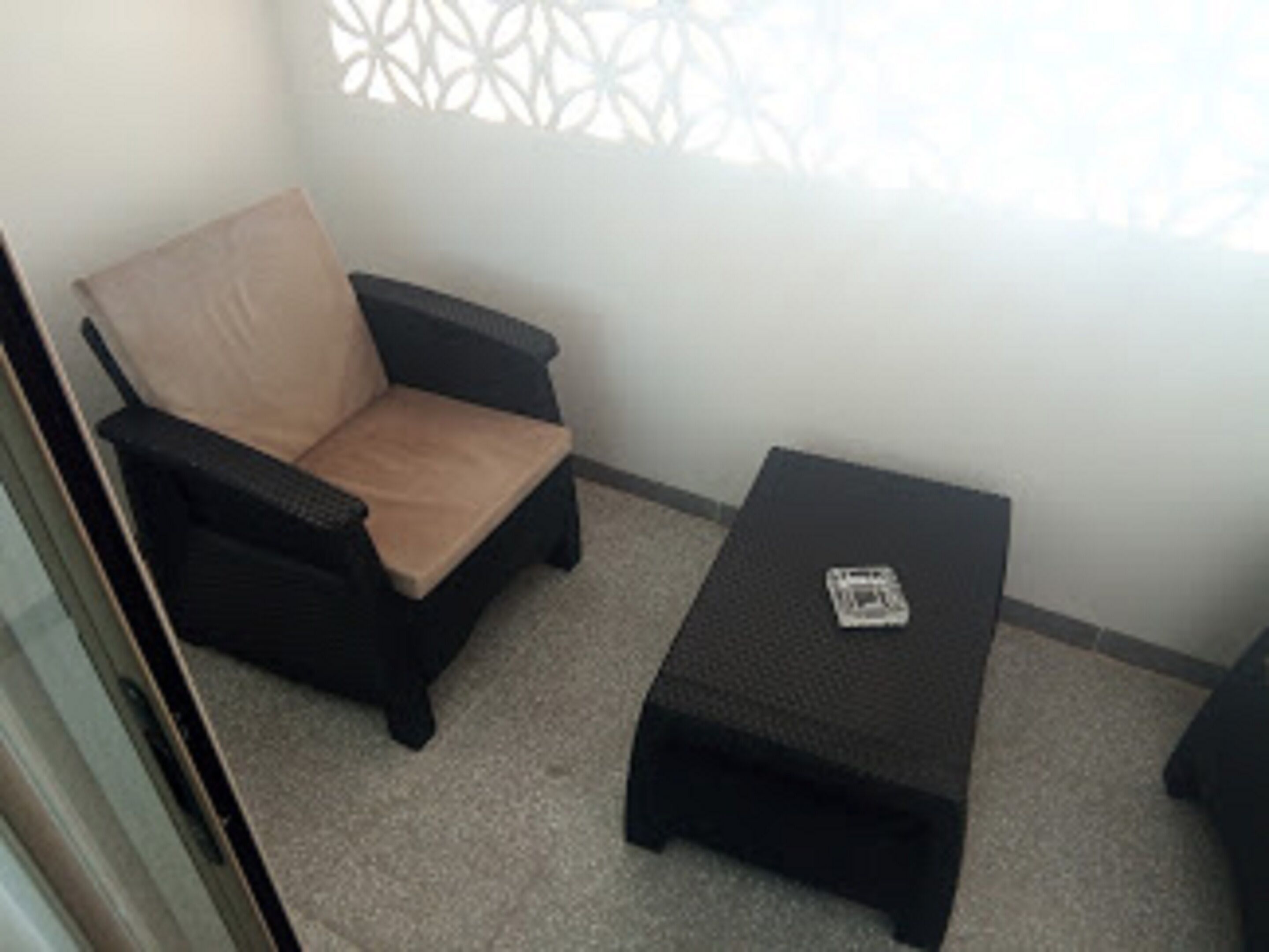 Un petit balcon avec une chaise en osier noir et une table assortie.