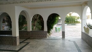A covered courtyard with arches, patterned floor tiles, and potted plants. - Hotel Souf (El Oued)
