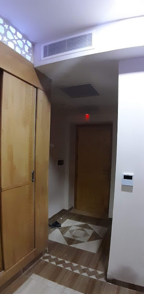 Un pasillo con un armario de madera, suelo estampado y una puerta con luz roja.
