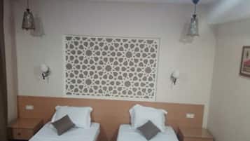Una habitación con dos camas, un panel decorativo en la pared y dos lámparas fijadas a la pared.