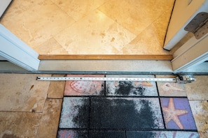 A measuring tape across a tiled floor with a starfish design and a wooden threshold.