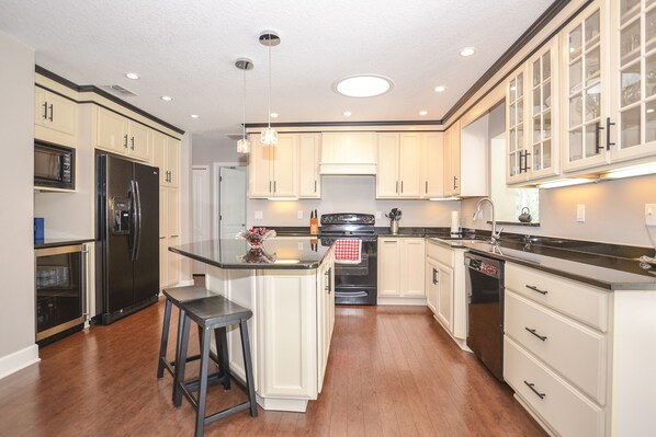 A modern kitchen with white cabinetry, a central island, stainless steel appliances, and pendant lighting. - Whispering Palms - Beach-Side Pool Home (Ponce Inlet)