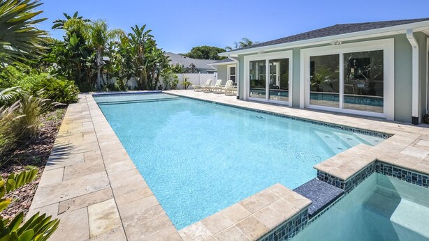 Una piscina rectangular amb aigua blava cristal·lina, envoltada per un sòcol de pedra i vegetació tropical exuberanta.