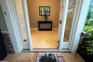 A door leading to a room with a tiled floor, a small console table with a vase of flowers, and a mirror on the wall.