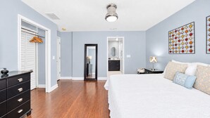 Une chambre à coucher avec un grand lit, une commode, un placard et une salle de bain visible à travers une porte ouverte.
