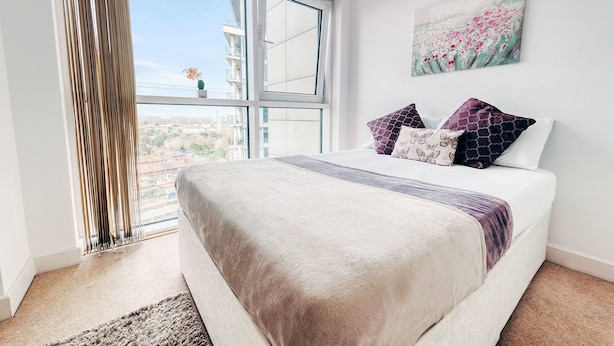 A bedroom with a large window, a bed with patterned pillows, and a painting on the wall. - Royal Modern Apartment (London)