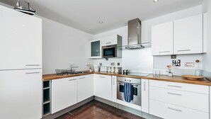 A modern kitchen with white cabinets, a wooden countertop, and stainless steel appliances. - Royal Modern Apartment (London)