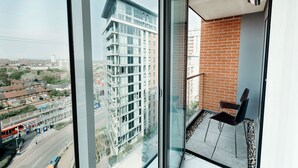 A high-rise building with a glass facade, a balcony with a chair, and a view of a cityscape. - Royal Modern Apartment (London)