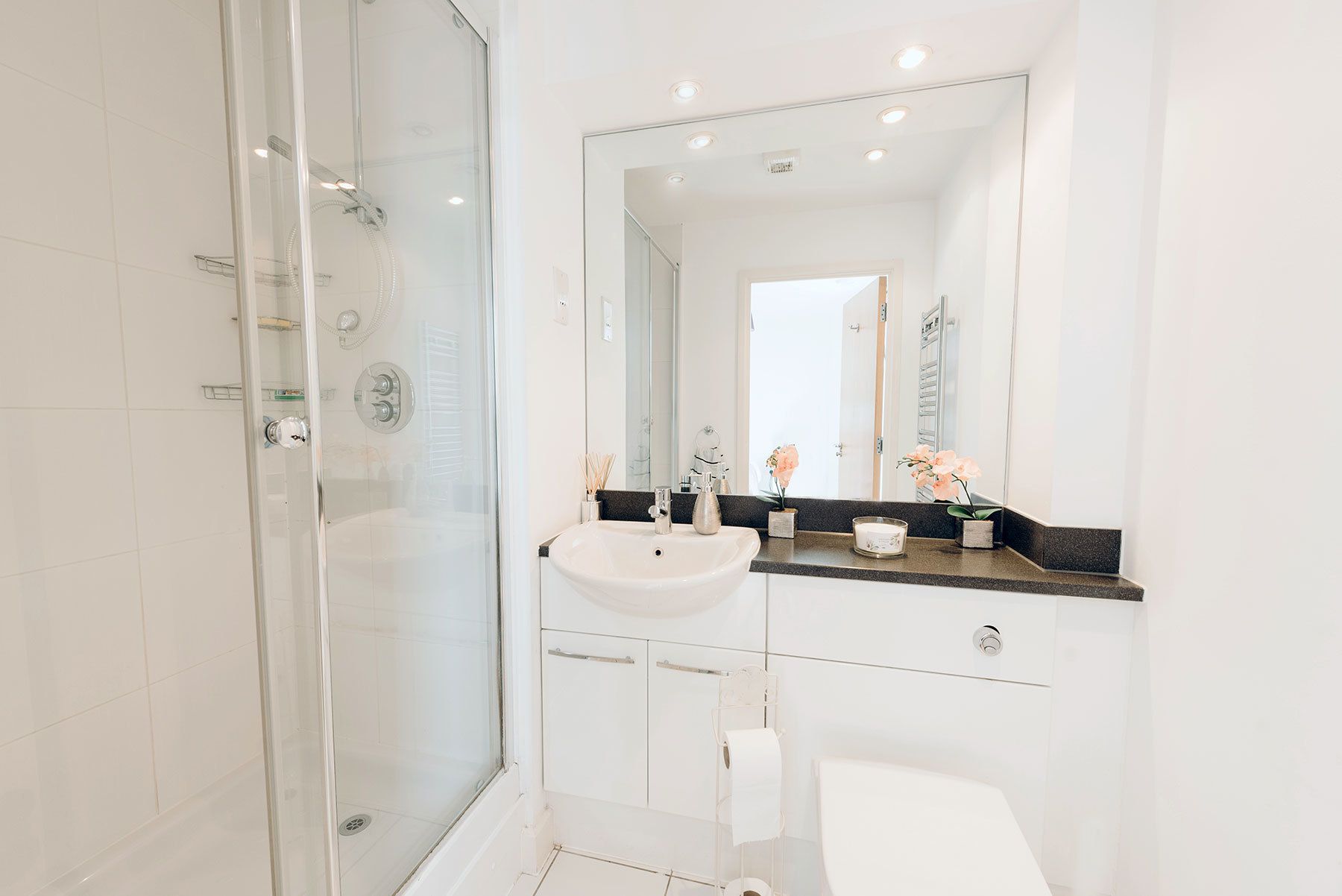 A modern bathroom with a glass-enclosed shower, a white sink, and a large mirror.
