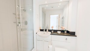 A modern bathroom with a glass-enclosed shower, a white sink, and a large mirror. - Royal Modern Apartment (London)