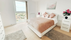 A bedroom with a large bed, a dresser, a nightstand, a window with a view, and a potted plant. - Royal Modern Apartment (London)