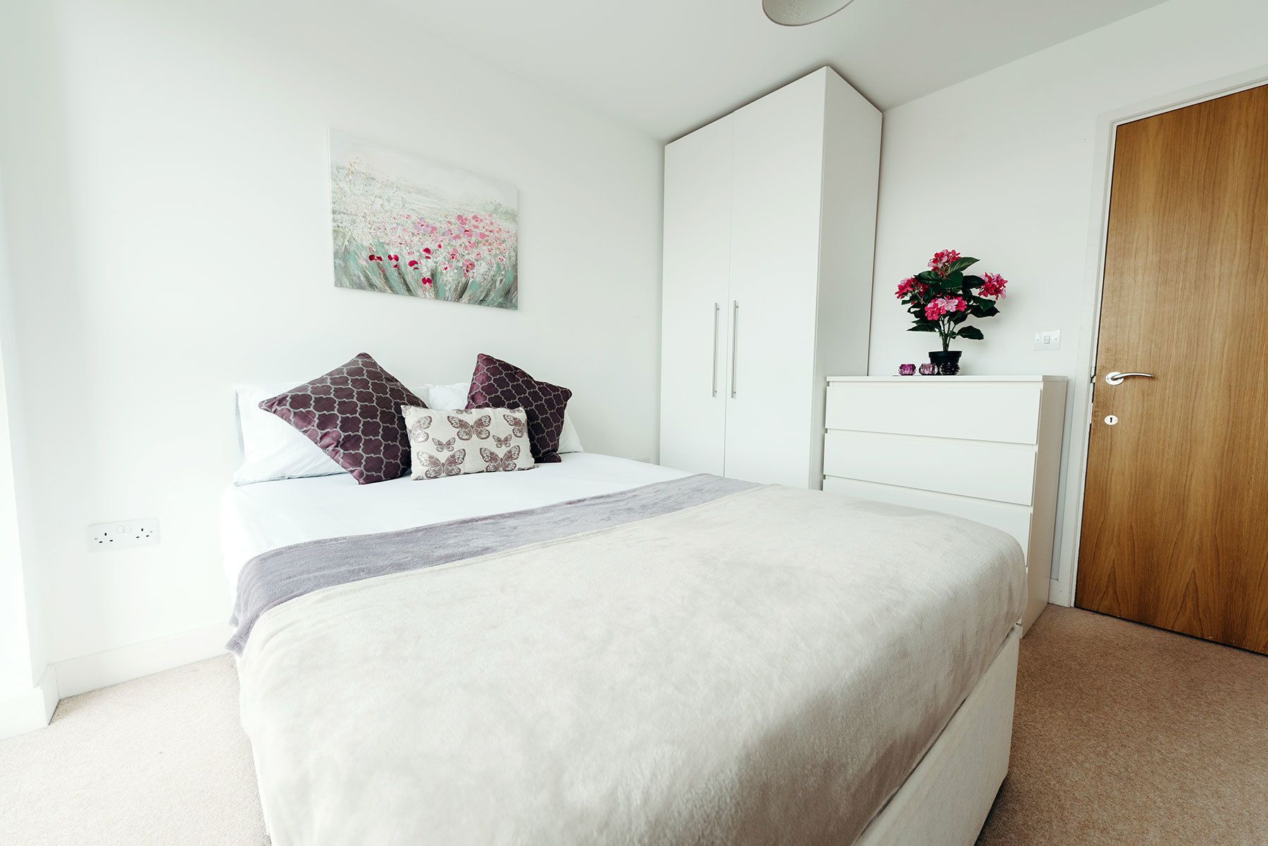 A bedroom with a bed, a wardrobe, a door, and a wall-mounted painting.