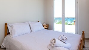 A hotel room with a bed, a nightstand, and a view of the sea through a sliding glass door. - Beach Front Villa Gousetis (Zakynthos)