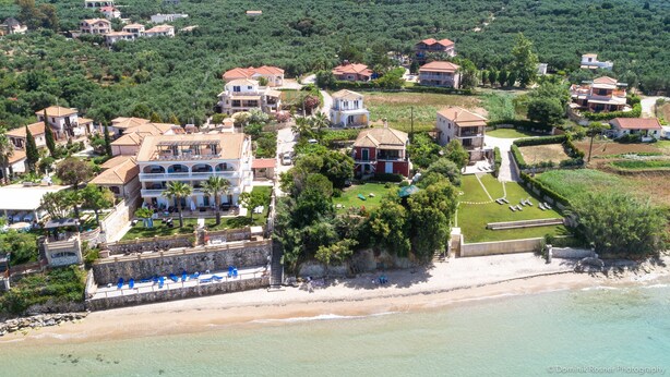 An aerial view of a coastal residential area with multiple houses, a beach, and a well-maintained lawn. - Beach Front Villa Gousetis (Zakynthos)