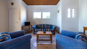 A living room with a wooden ceiling, a sofa, two armchairs, a coffee table, and a television on a stand. - Beach Front Villa Gousetis (Zakynthos)