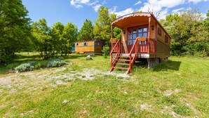 A wooden cabin with a porch and steps, surrounded by lush greenery and trees. - La Grange d'Emile Gites, Roulottes et Piscine (Blandas)