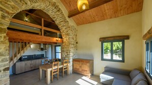 A rustic kitchen with stone walls, wooden beams, and a dining area with a sofa and table. - La Grange d'Emile Gites, Roulottes et Piscine (Blandas)