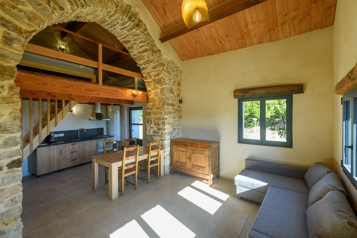 A rustic kitchen with stone walls, wooden beams, and a dining area with a sofa and table.