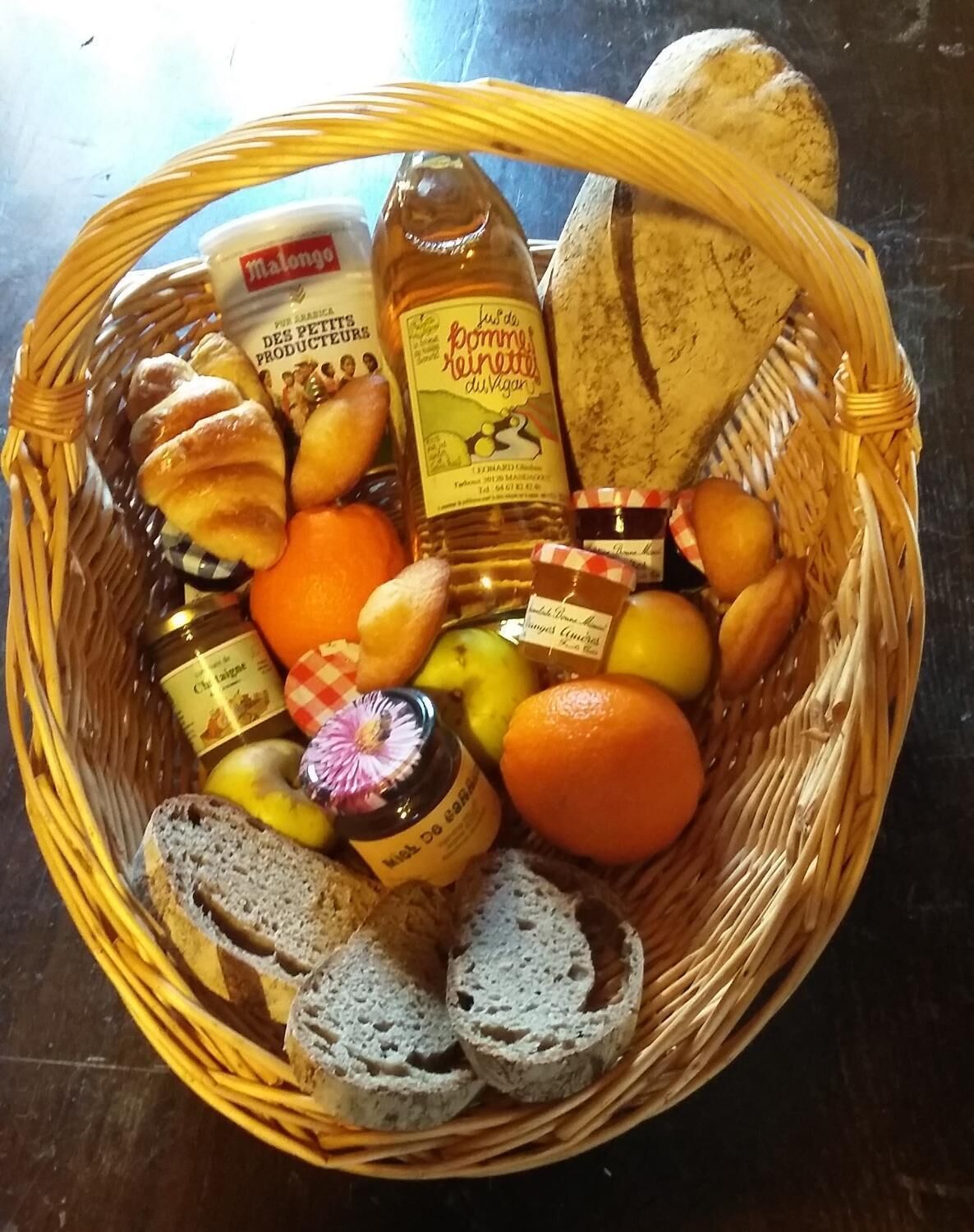 A wicker basket containing various food items including bread, oranges, and jars of preserves.