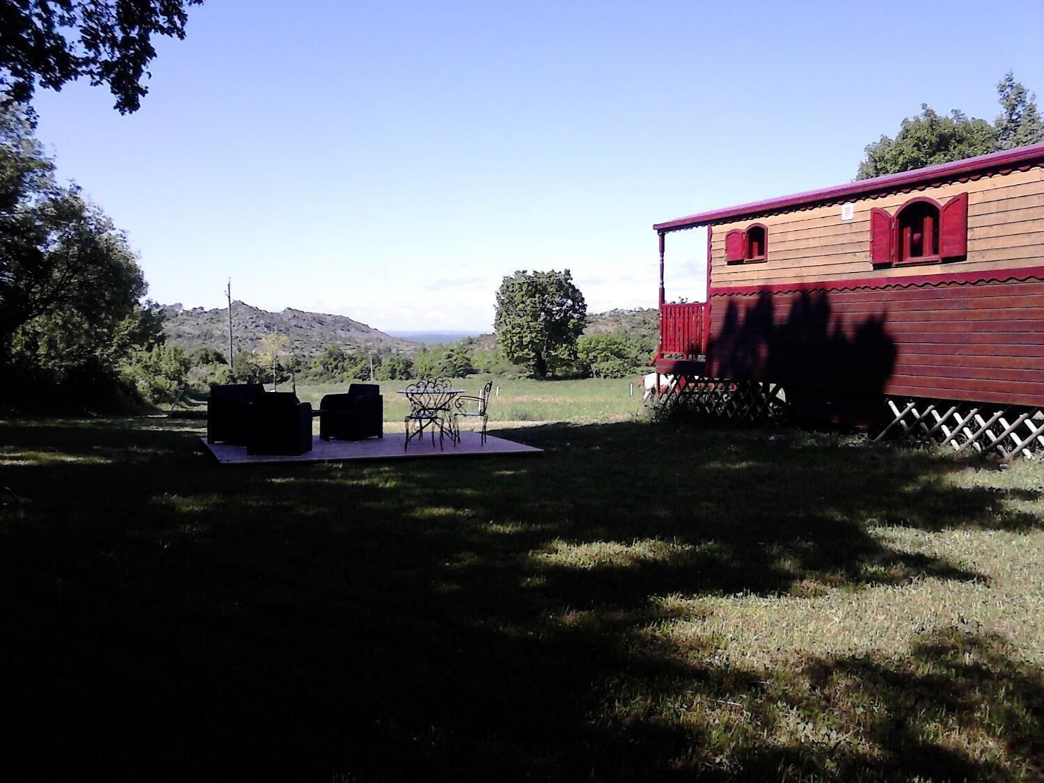 Una casa in legno con tetto rosso e un balcone, immersa nel verde con un tavolo e sedie.