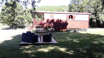 Une cabane en bois à l’extérieur rouge, dotée d’une terrasse et d’une table de pique-nique avec des chaises.