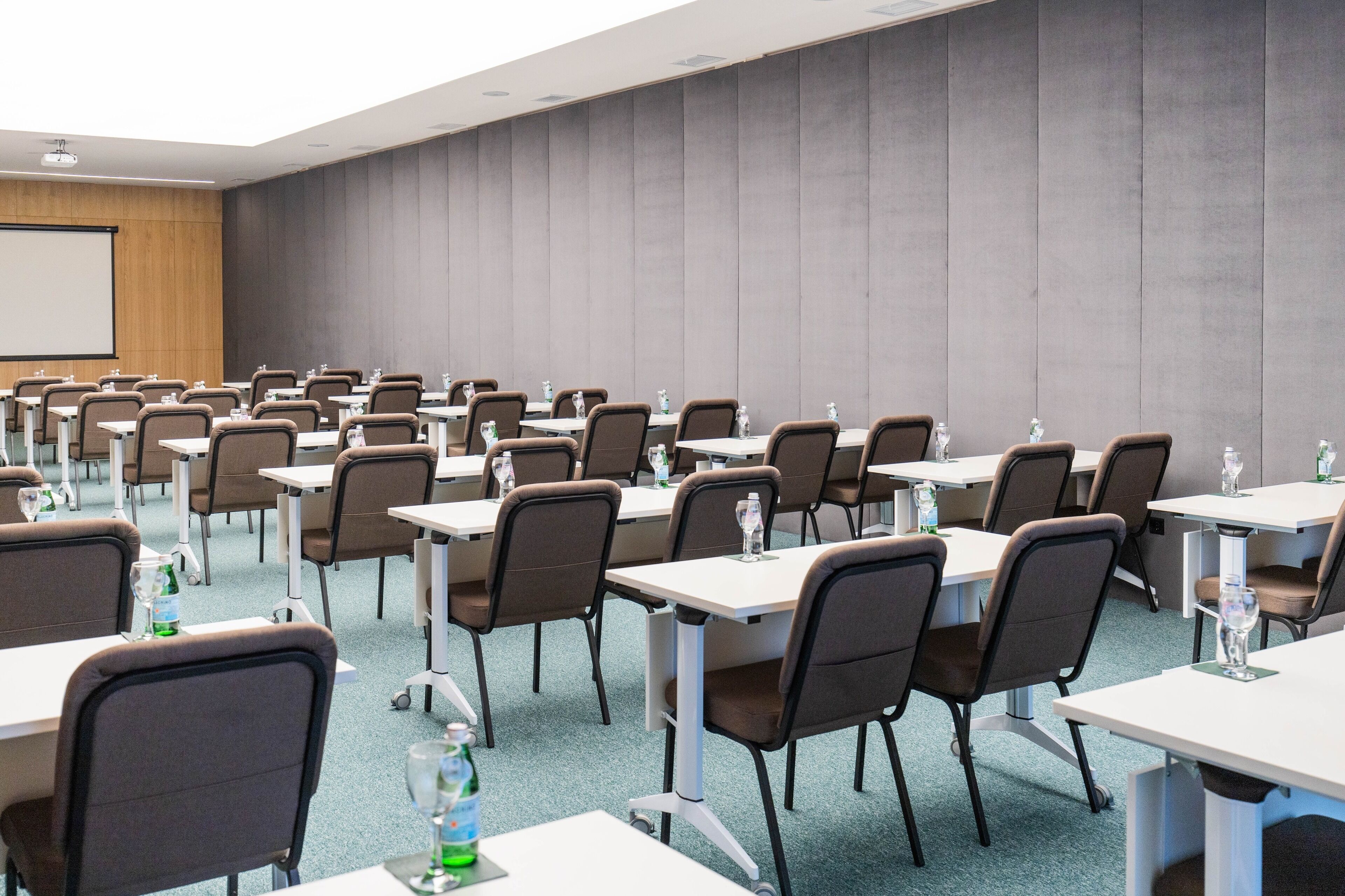 Un salón de conferencias con filas de mesas y sillas, equipado con botellas de agua y vasos.