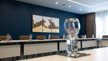 Un salón de conferencias con una larga mesa, sillas y un micrófono. Hay botellas de agua sobre la mesa.