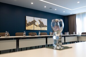 Un salón de conferencias con una larga mesa, sillas y un micrófono. Hay botellas de agua sobre la mesa.