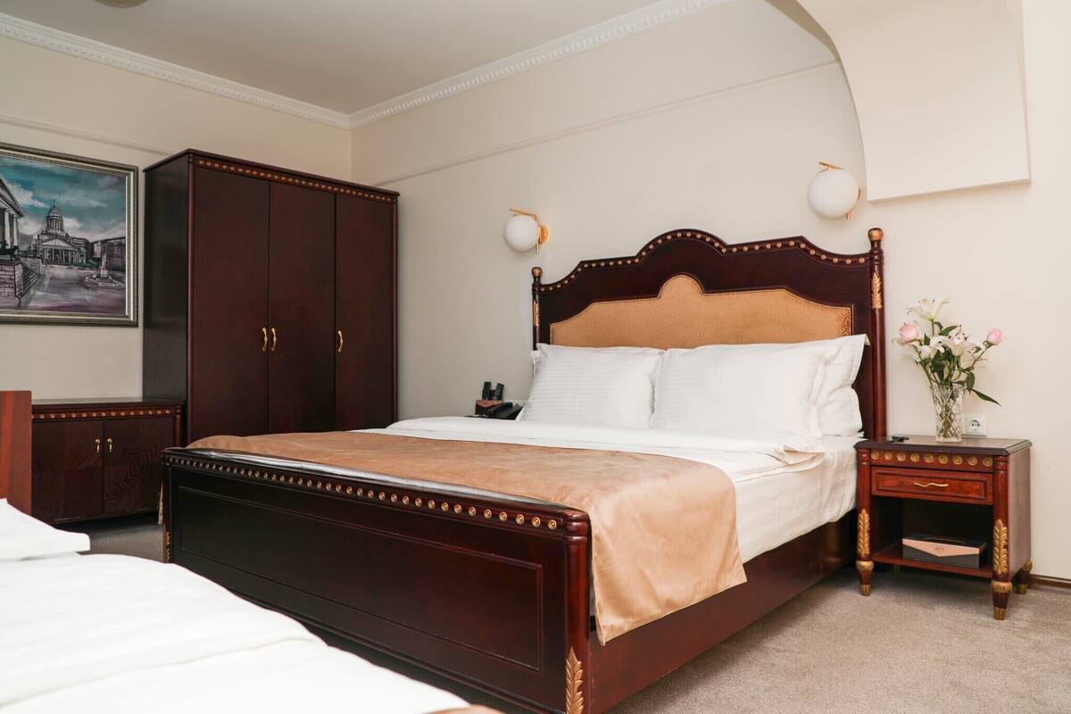 A neatly arranged bedroom with a large bed, a wardrobe, a bedside table with a lamp, and a framed picture on the wall.