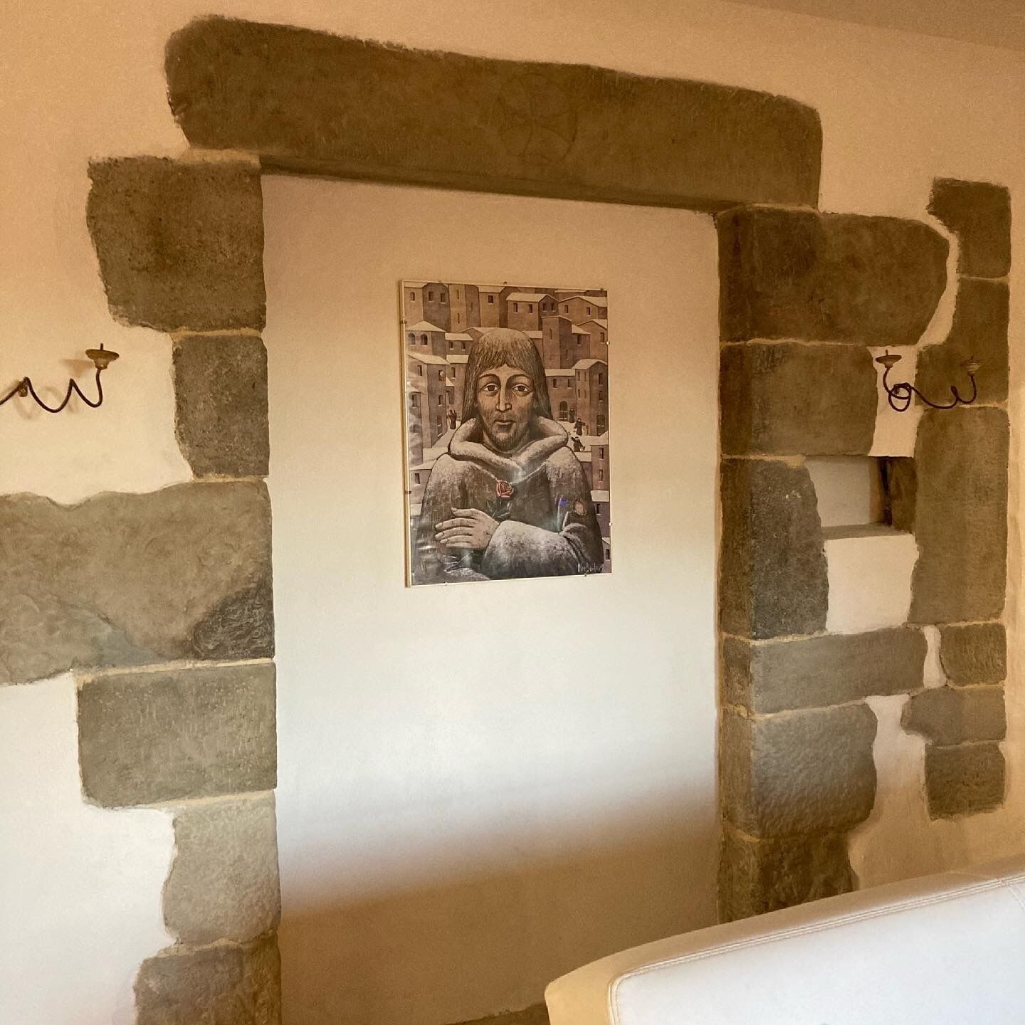 Una obra de arte enmarcada sobre una pared de piedra, con dos apliques a cada lado.
