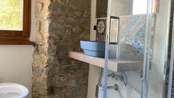 A bathroom with a stone wall, a tiled floor, a white sink, and a glass shower enclosure.