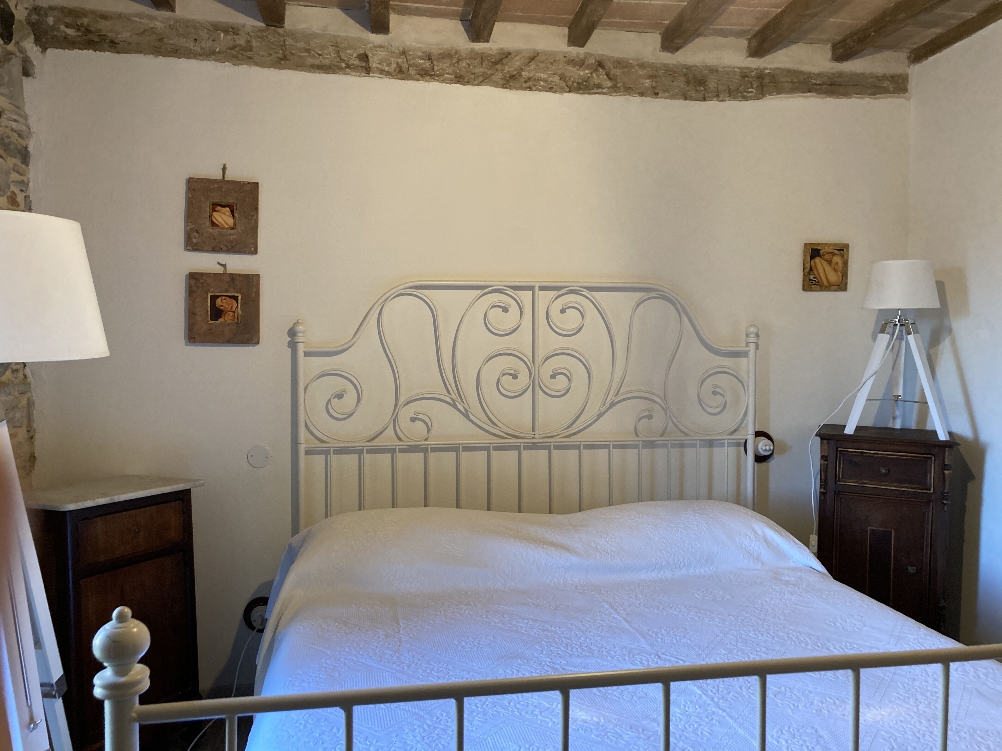 Un dormitorio con estructura de cama metálica, una mesita de noche de madera, una lámpara y un armario pequeño.