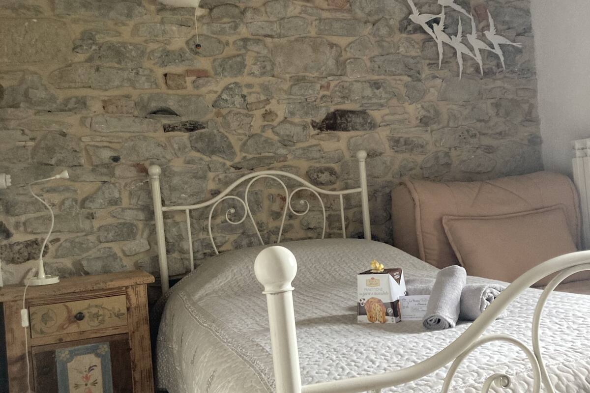 Un dormitorio con pared de piedra, cama con cabecera blanca, mesita de noche y un aparador.